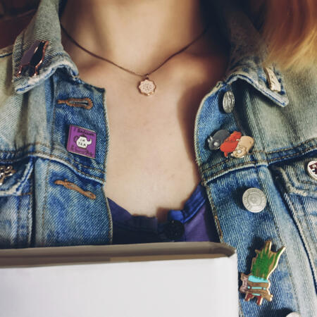 Photo of Maisie's neck and chest. She is white, wearing a blue denim jacket over a dress, and holding a hardback book.